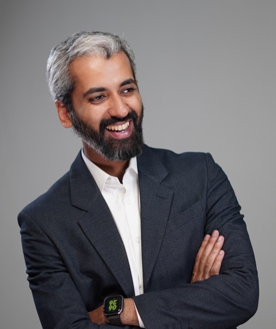 Sameer Ahmed Khan, colour studio portrait, navy blazer and white shirt, laughing, arms crossed